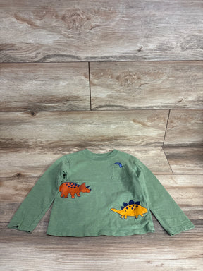 Green long-sleeve toddler shirt with colorful dinosaur prints and small pocket on wooden floor