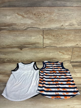 Flat lay of two toddler tank tops (size 4-5T): solid white with black trim and navy-and-white stripes with orange tie-dye, on wood background