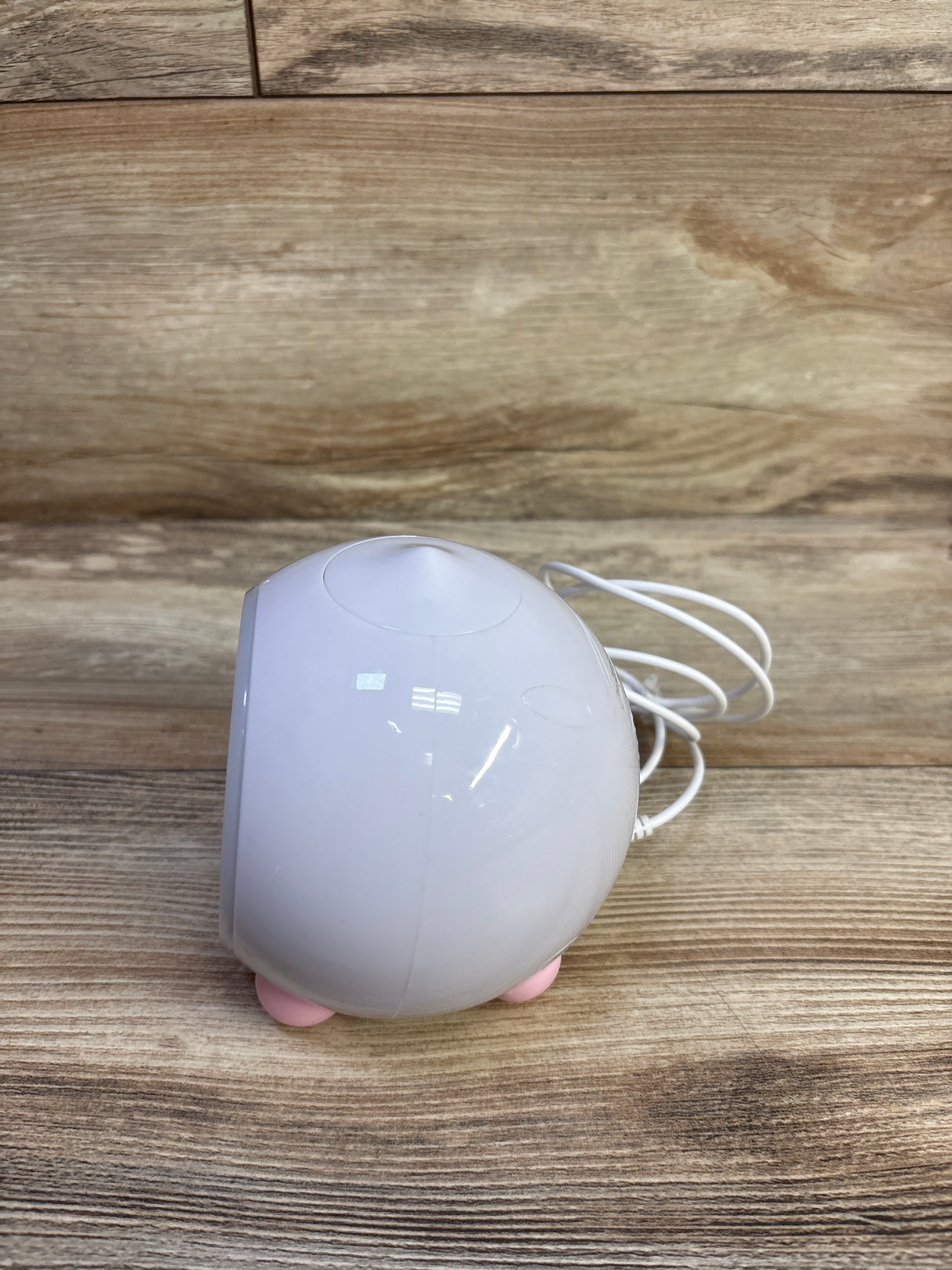 Side view of LittleHippo Mella sleep trainer clock with white rounded body, pink feet, and coiled cord on wood