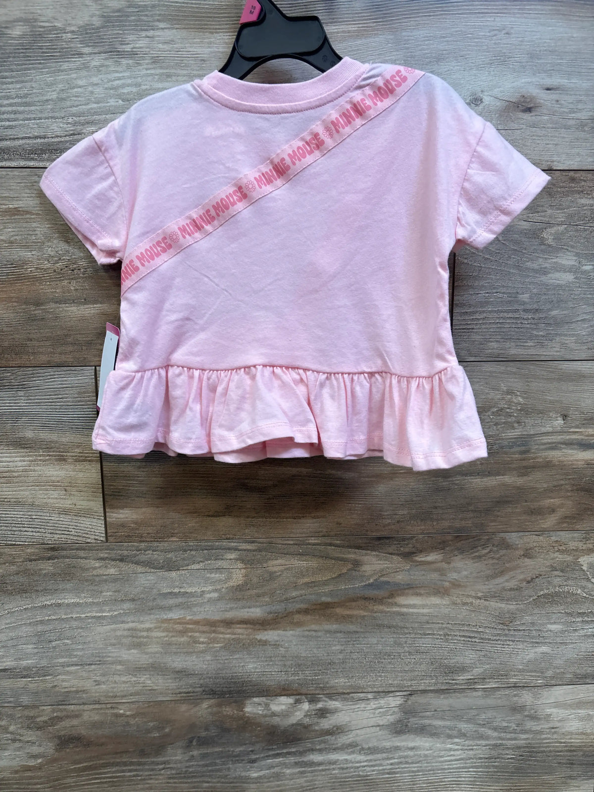 Front view of pink Disney Junior Minnie Mouse shirt with diagonal lettering and gathered ruffle hem on a hanger
