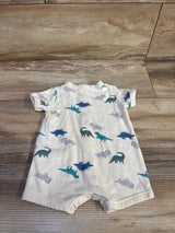 Back view of white shortie romper showing blue and teal dinosaur print and snap crotch, laid flat on wood floor