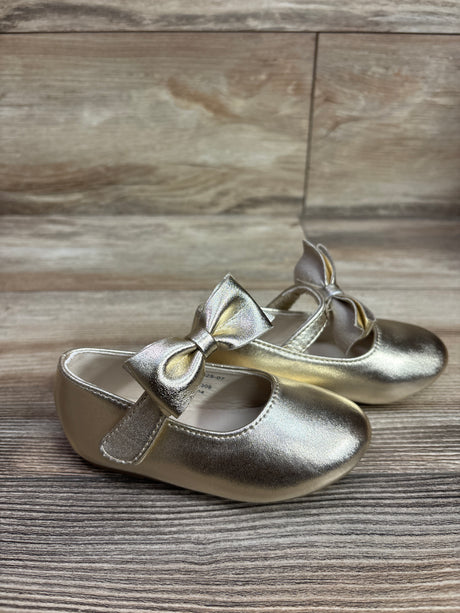 Front and side view of Felix & Flora Mary Jane bow dress flats in gold, showing ankle straps and bows on wood-grain surface