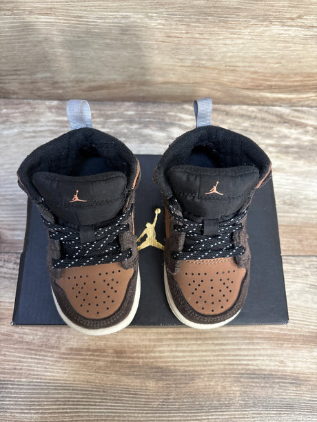 Brown and black toddler sneakers with perforated toes on a box, displayed on wood floor