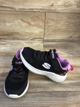 Side view of black Skechers toddler sneaker with pink floral heel, white ridged sole, elastic laces and velcro strap on wood floor
