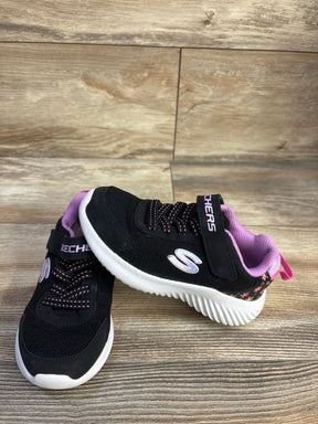Side view of black Skechers toddler sneaker with pink floral heel, white ridged sole, elastic laces and velcro strap on wood floor