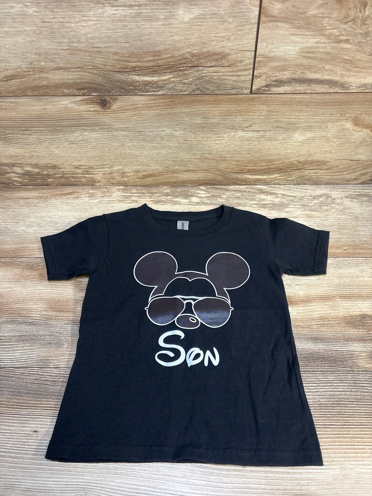 Black kids t-shirt with cartoon mouse face in sunglasses and 'Son' text, laid on wood