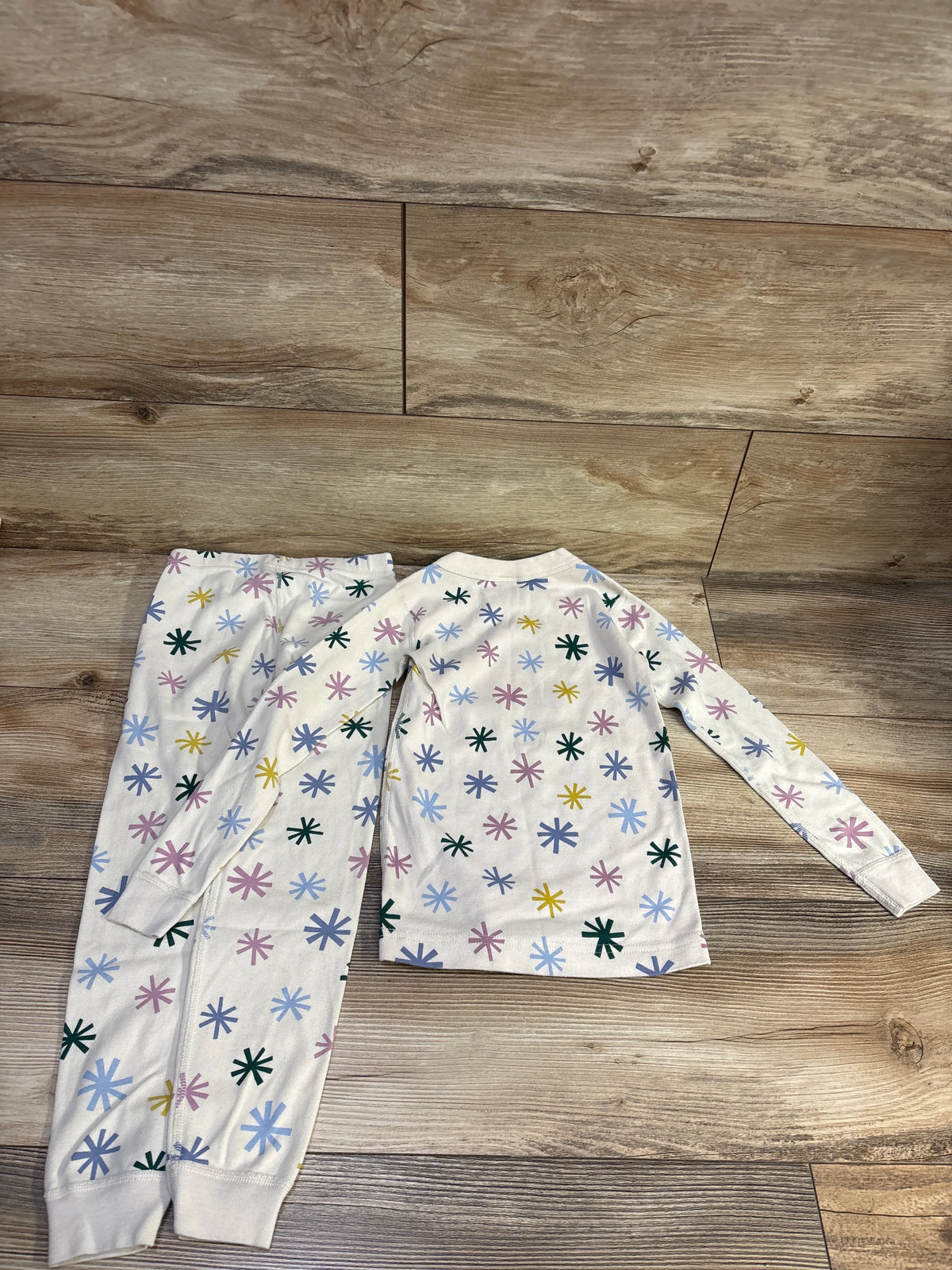 Top view of Hanna Andersson two-piece organic long johns pajama set in ivory with multicolor starburst pattern on wood floor