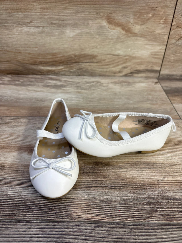 Angled front view of Cat & Jack Nora white slip-on ballet flats showing bow, elastic strap and polka-dot insole on wood floor