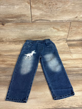 Front flat lay of toddler blue jeans with white T-Rex patch on left thigh, faded knees and elastic waist on wood floor