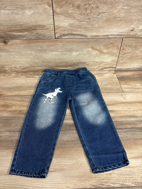 Front flat lay of toddler blue jeans with white T-Rex patch on left thigh, faded knees and elastic waist on wood floor