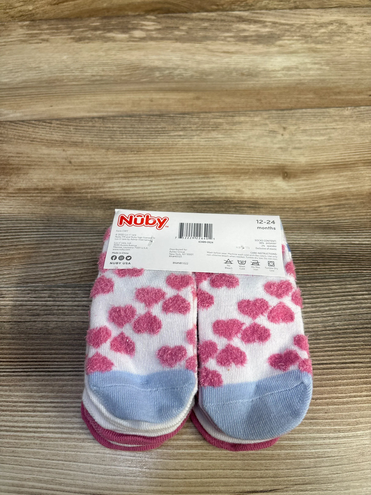 Front view of Nuby 10-pack baby socks showcasing pink heart pattern, blue toe accents, and size label 12-24 months on a wood surface