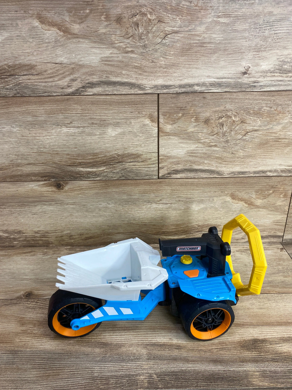 Matchbox toy dump truck with white bucket, blue body, black and orange wheels, and yellow handle on wood surface