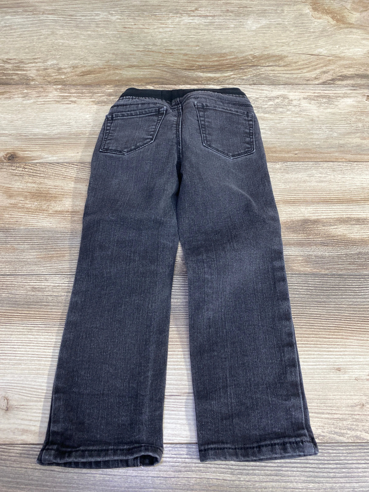 Children's black denim jeans with pockets, laid flat on wooden background