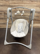 Front view of Graco Slim Spaces Compact Baby Swing in Reign with padded seat, safety harness, and hanging plush toys