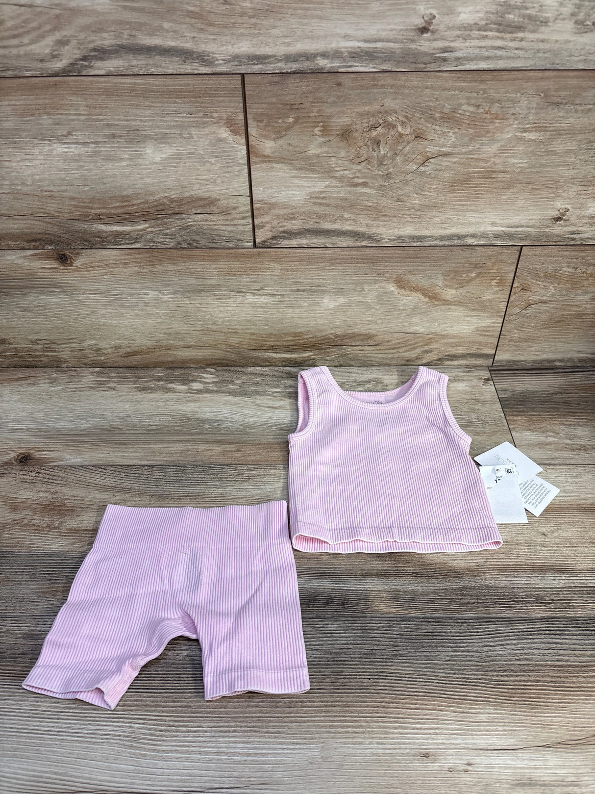 Flat lay of Grayson mini ribbed tank top and matching bike shorts in pink, size 12 months, showing ribbed texture on wood background