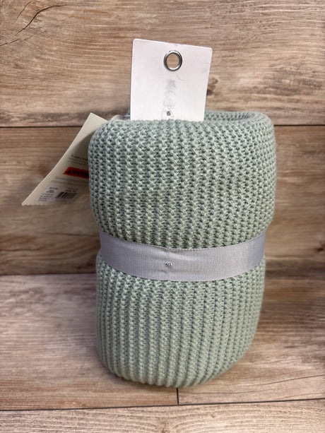 Close-up of rolled Cloud Island knit baby blanket in sage green showcasing ribbed knit texture and gray ribbon on wooden background