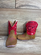 Front and side view of Tin Haul mini square-toe toddler boots showing brown faux-leather foot, red sparkly paisley shaft and soft pink sole on wood background