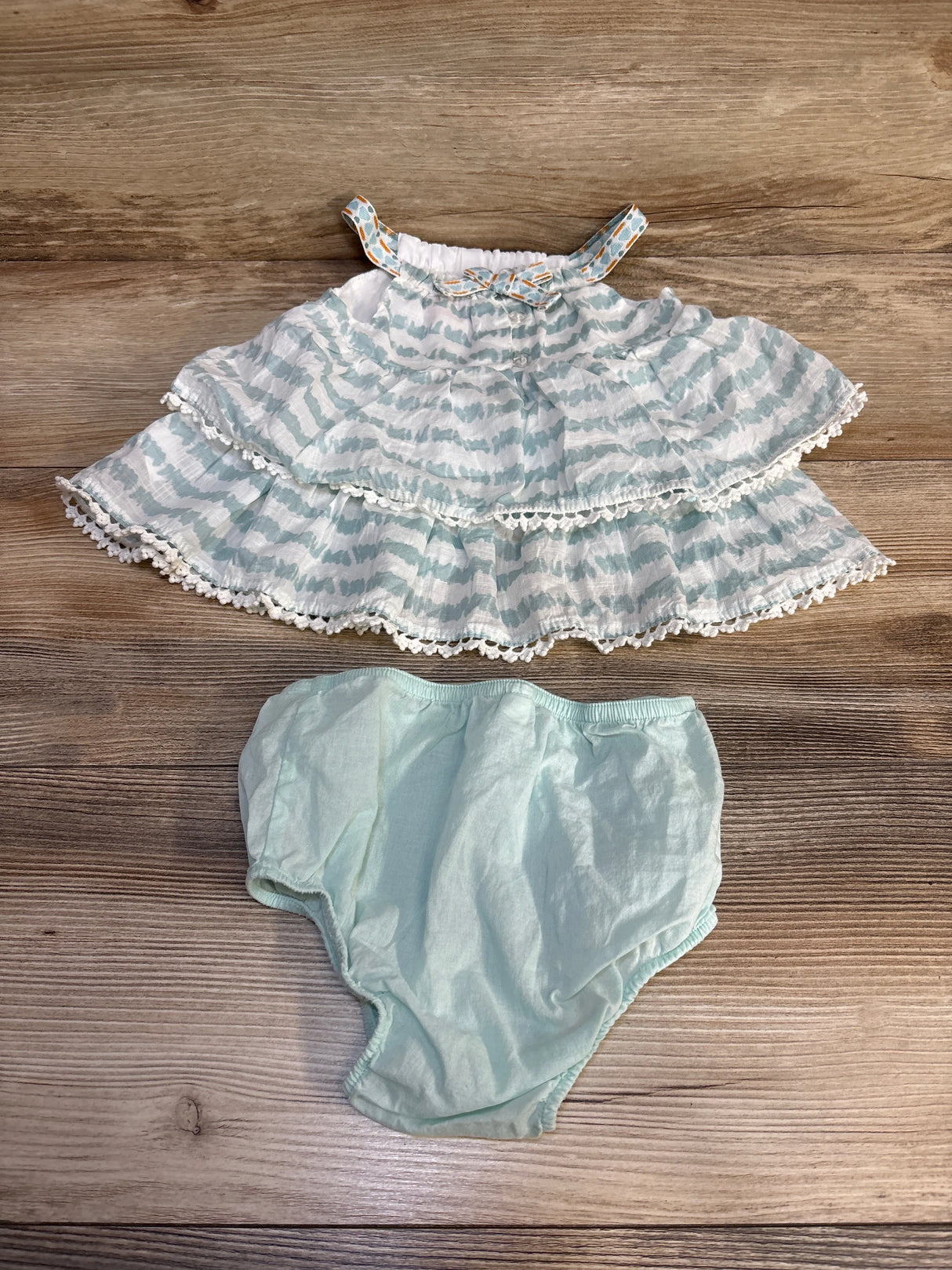 Baby girl's mint green patterned ruffle top with matching bloomers, laid on wood floor