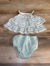 Baby girl's mint green patterned ruffle top with matching bloomers, laid on wood floor