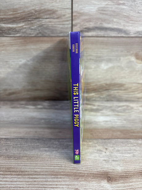 Spine view of This Little Piggy board book showing purple spine with vertical title and small pig icon on wood background