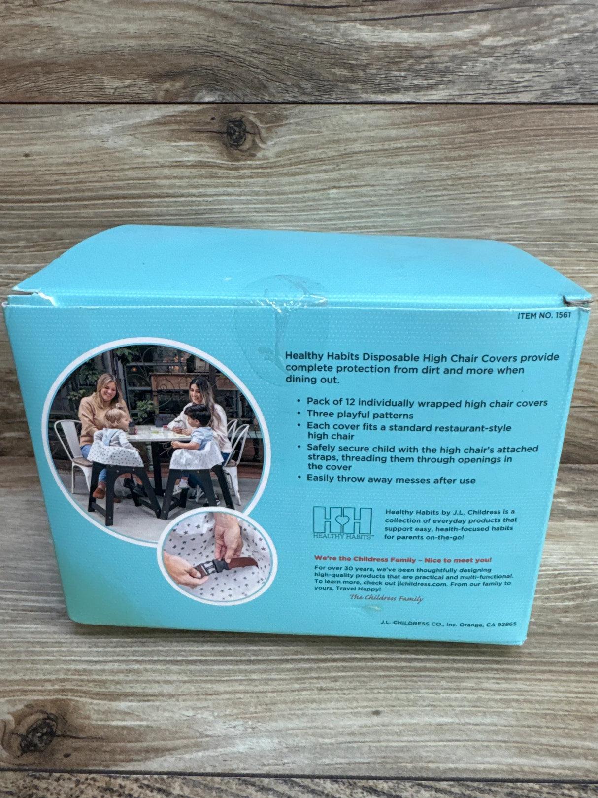 Back of J.L. Childress high chair cover box showing product text, photo of covers on chairs, and strap buckle on wood surface