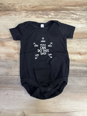 Front flat-lay of black 3-6M baby bodysuit showing white YOU CAN DO THIS DAD graphic with arrows on light wood background