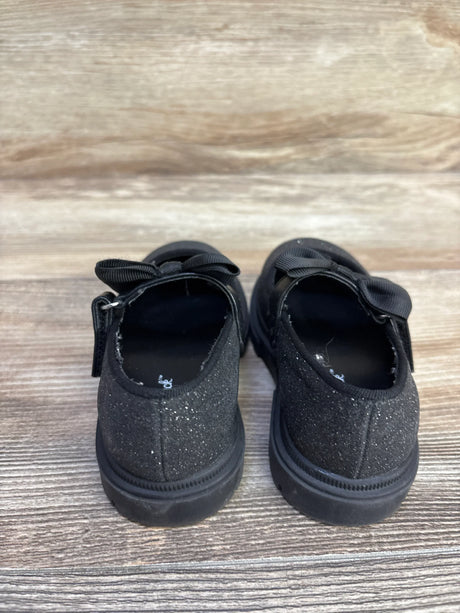 Rear view of Cat & Jack Kori lug-sole Mary Jane flats in black glitter showing bow strap and lug sole on wood background