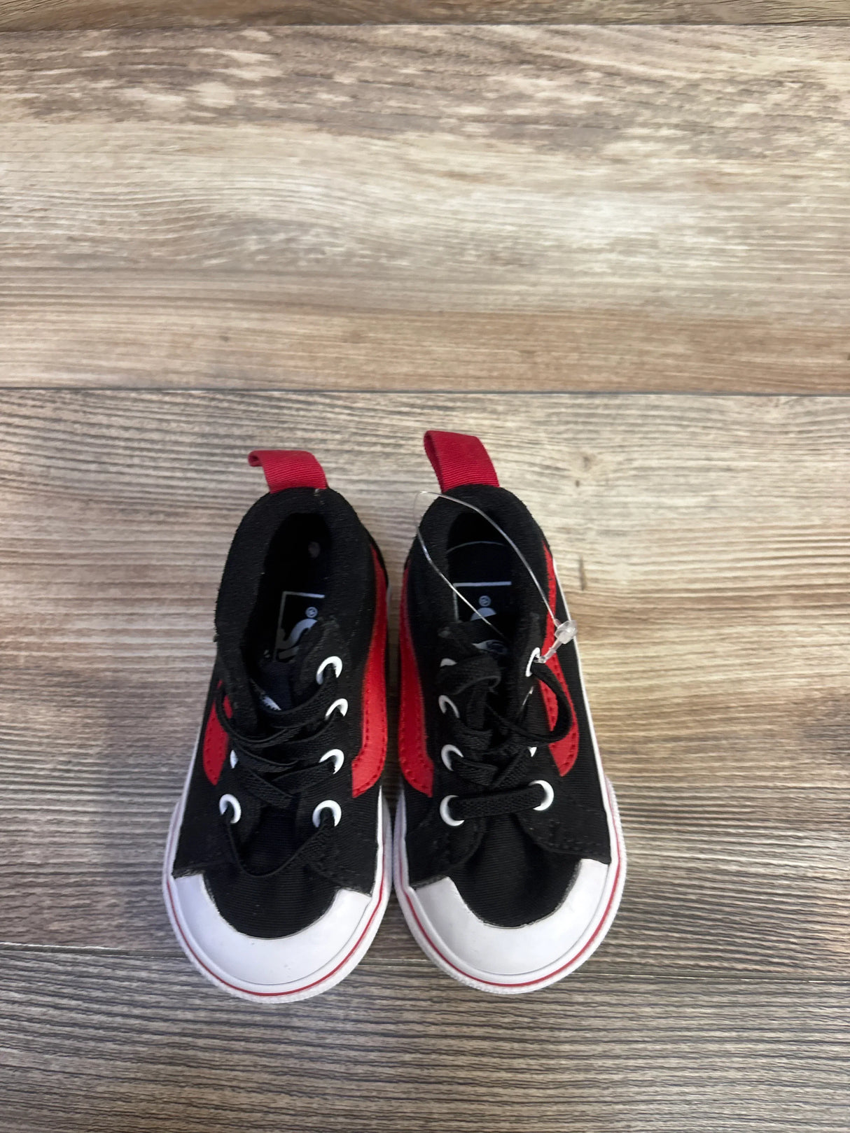 Top-down view of toddler Vans Racer Mid sneakers in black with red side panels, white rubber toe and sole, laces, on wood floor