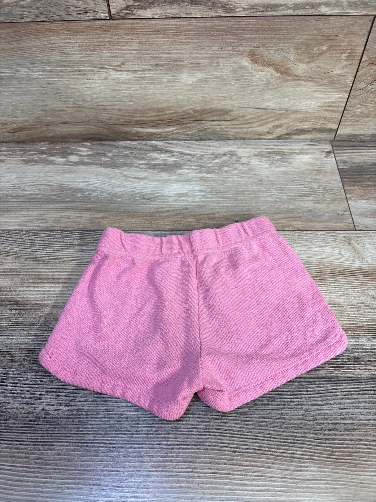 Top view of toddler pink terry shorts showing elastic waistband and soft terry texture on wood floor background