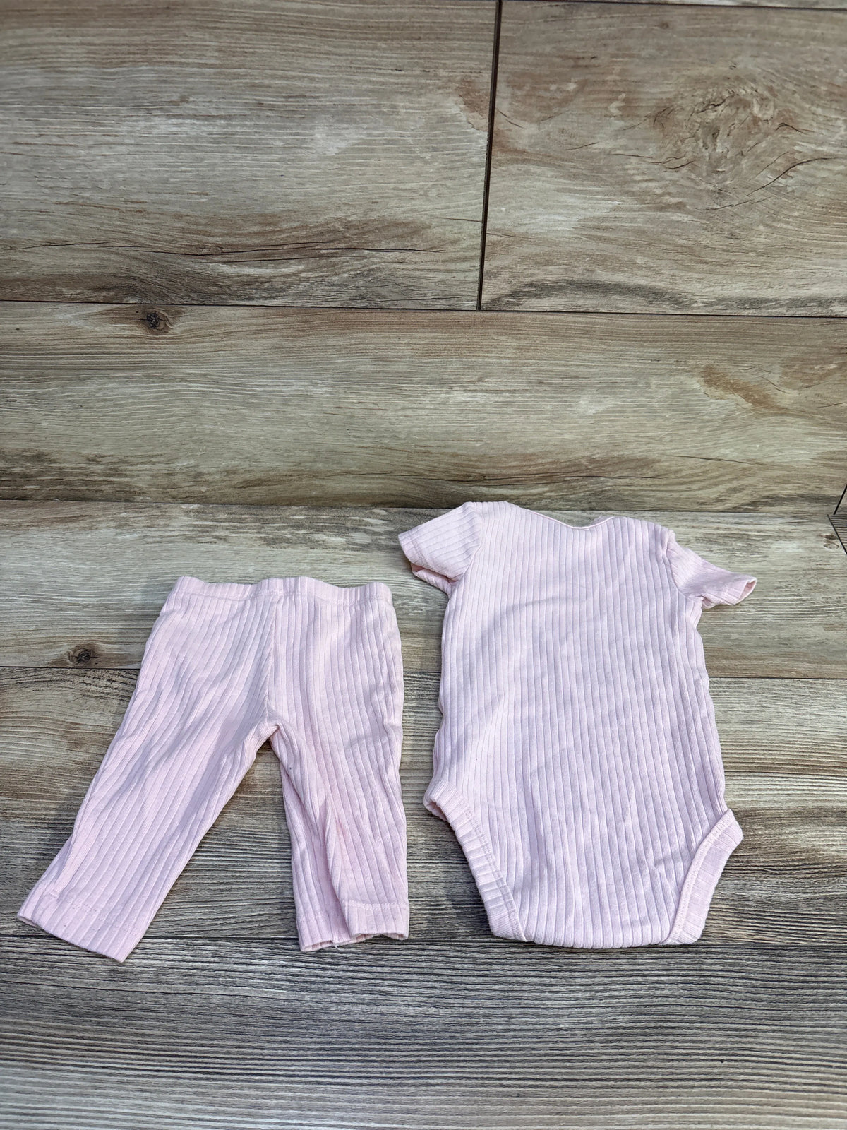 Flat lay of a pink ribbed bodysuit and pants set showcasing vertical ribbing with a wood-look background