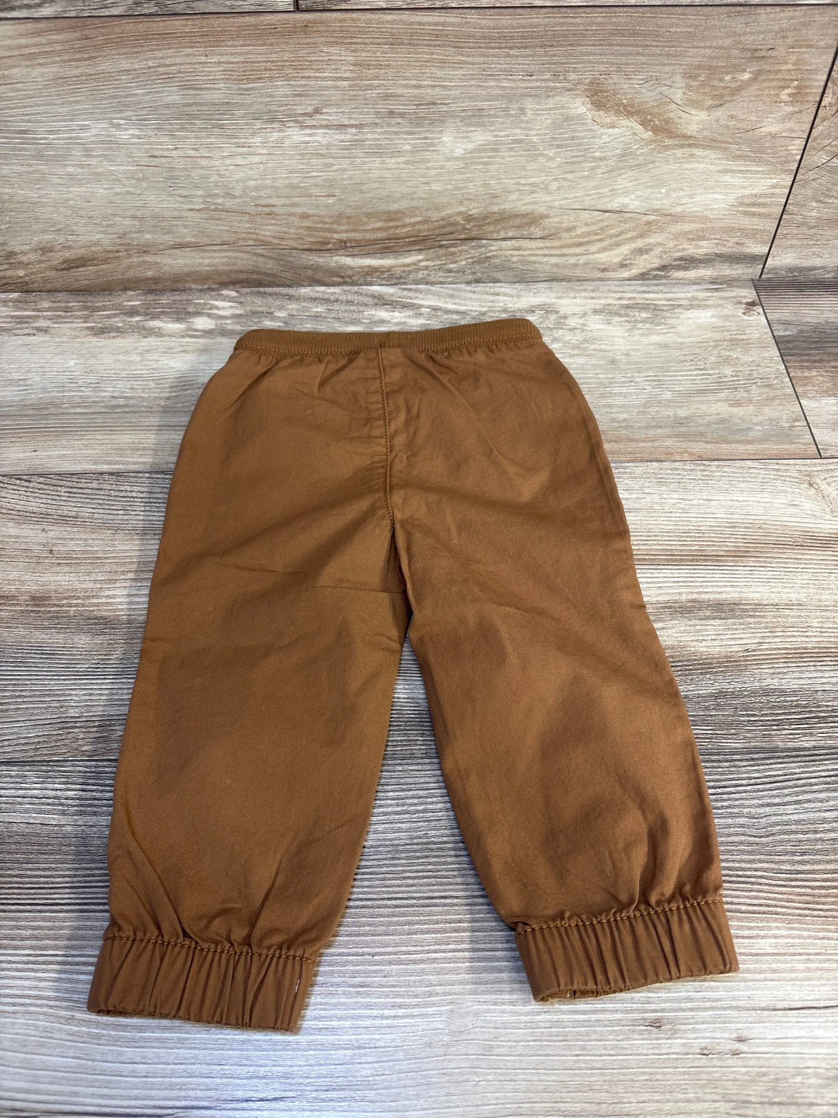 Flat lay of NEW Jumping Beans Pull-On Twill Joggers in Elgin beige with elastic waist and cuffed ankles sz 12m on wood plank floor