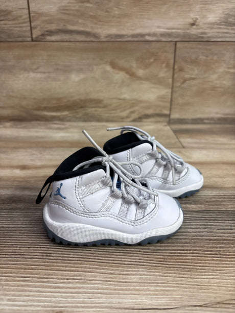 Three-quarter view of Air Jordan 11 Retro TD sneakers showcasing white uppers and blue accents with wood flooring