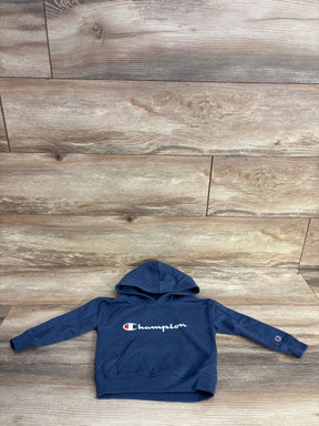 Navy blue Champion hoodie with front pocket and logo, laid flat on wood floor