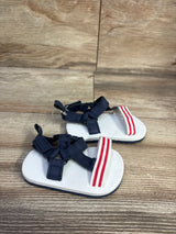 Front view of Child Of Mine baby sandals showcasing navy fabric straps and red and white striped toe band on wood floor background