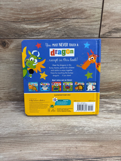 Back cover of Never Touch a Dragon board book showing colorful dragon illustrations and headline “You must never touch a dragon...except in this book” on a wood surface