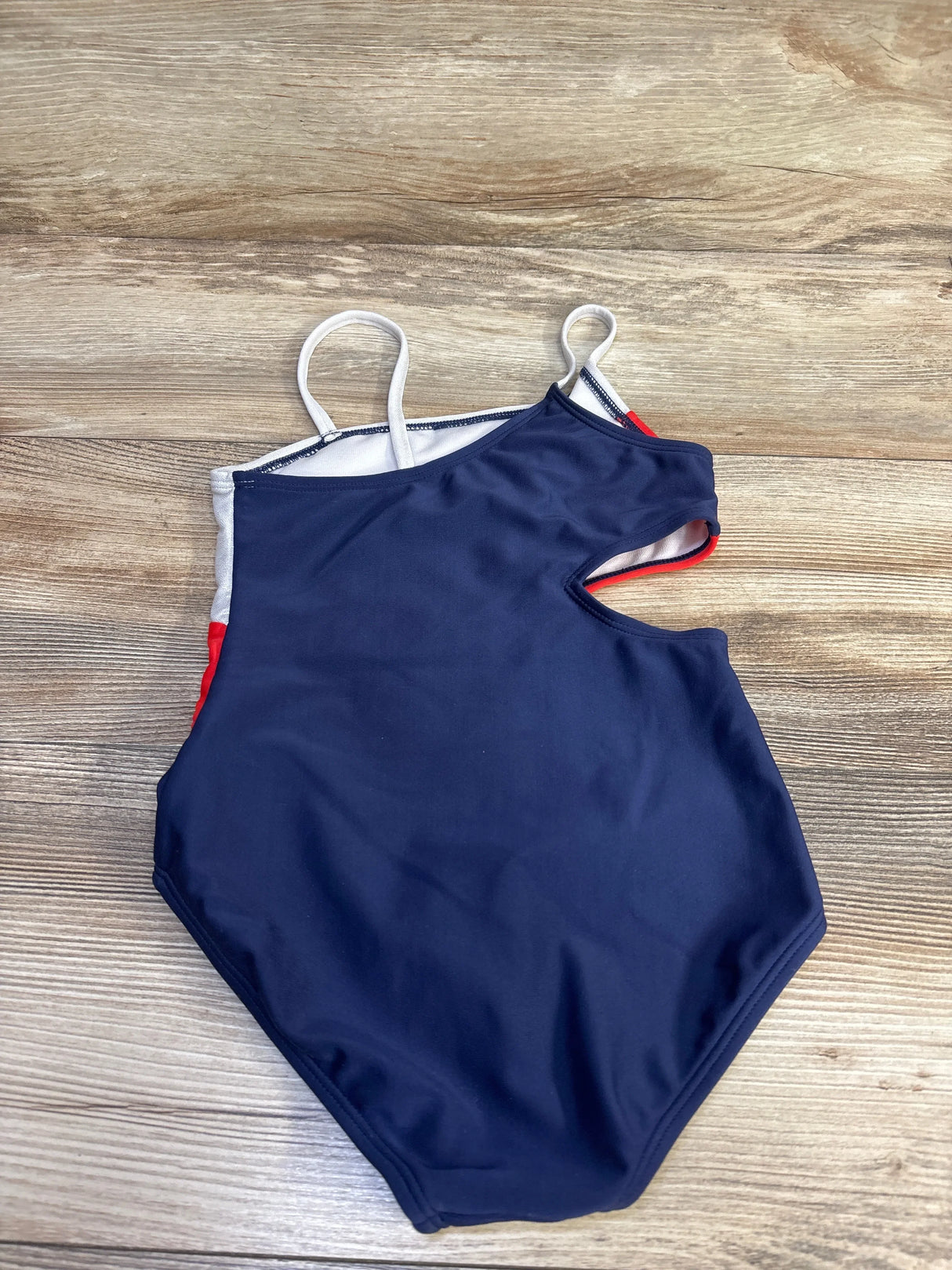 Flat lay of girls' red white and blue one-piece swimsuit showing front with side cut-out and white straps on wood background