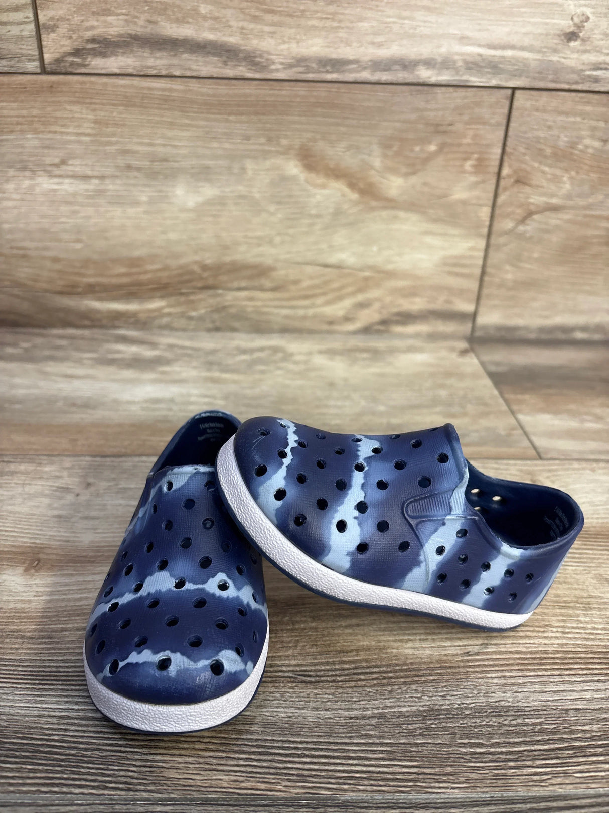 Three-quarter view of Cat and Jack slip-on toddler water shoes in navy tie-dye showing perforated upper and white sole on wooden floor