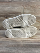 Bottom view of gently used kids sneakers with white rubber soles on wood floor
