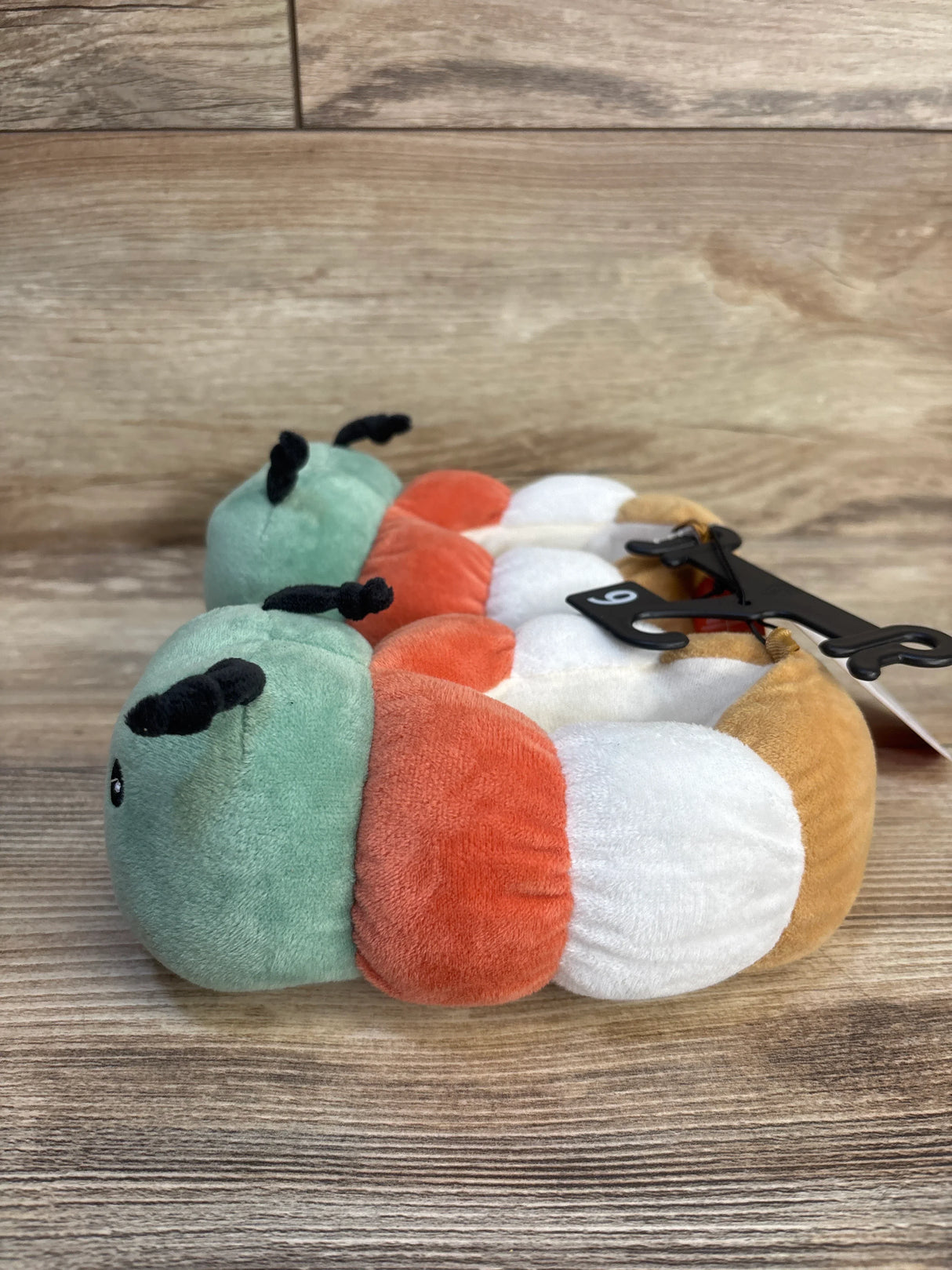 Colorful caterpillar plush toy with soft segments and black antennae on wooden surface