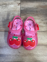Top view of Cat & Jack pink cherry jelly sandals with red cherry appliques, heart-print insoles on wood floor