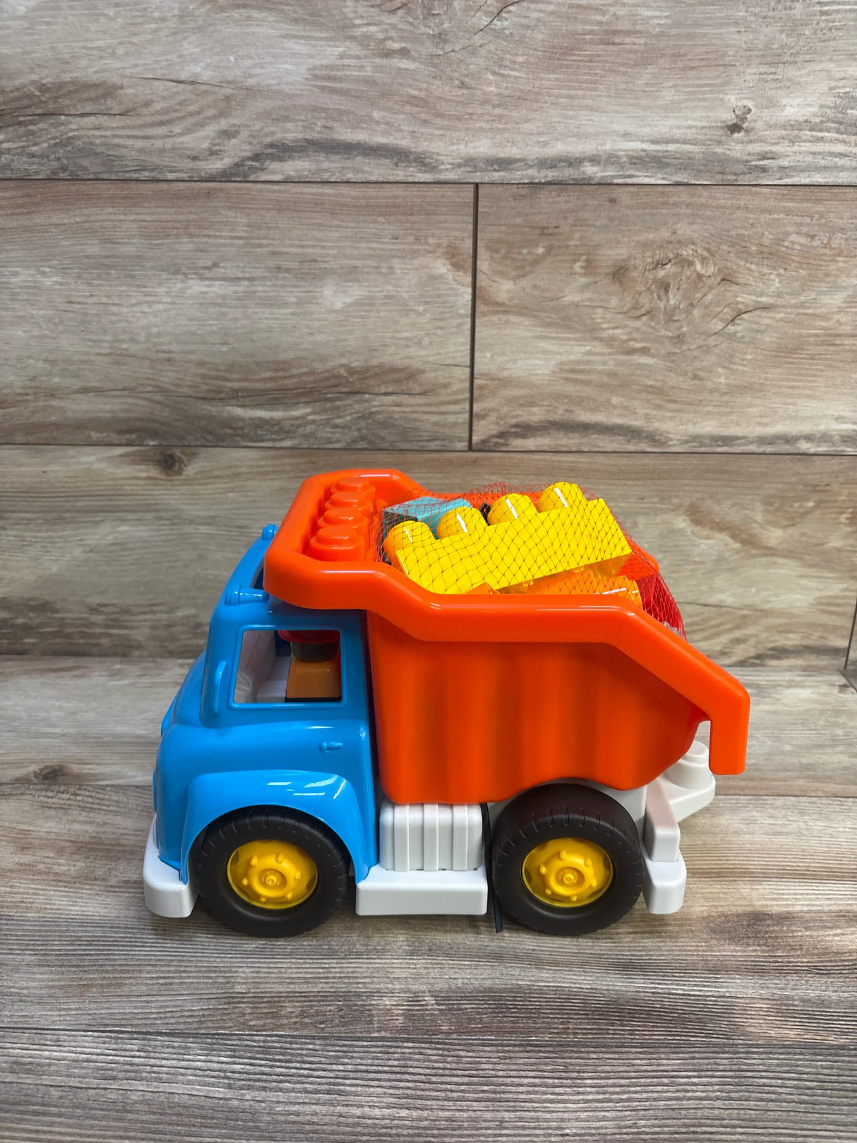 Side view of Battat dump truck with building blocks showcasing blue cab, orange bed, and yellow wheels on a wood-grain background