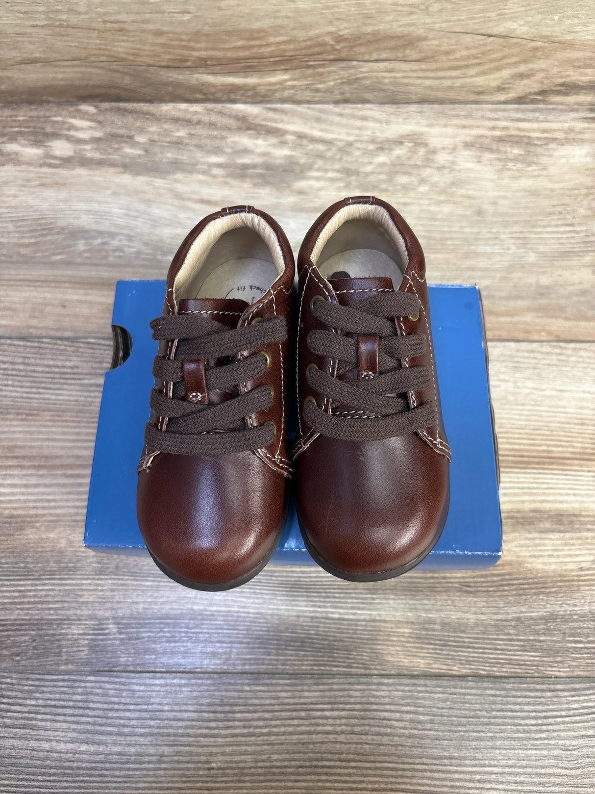 Top view of Stride Rite SRTech Elliot toddler brown leather sneakers, lace-up with white stitching on blue box and wood floor