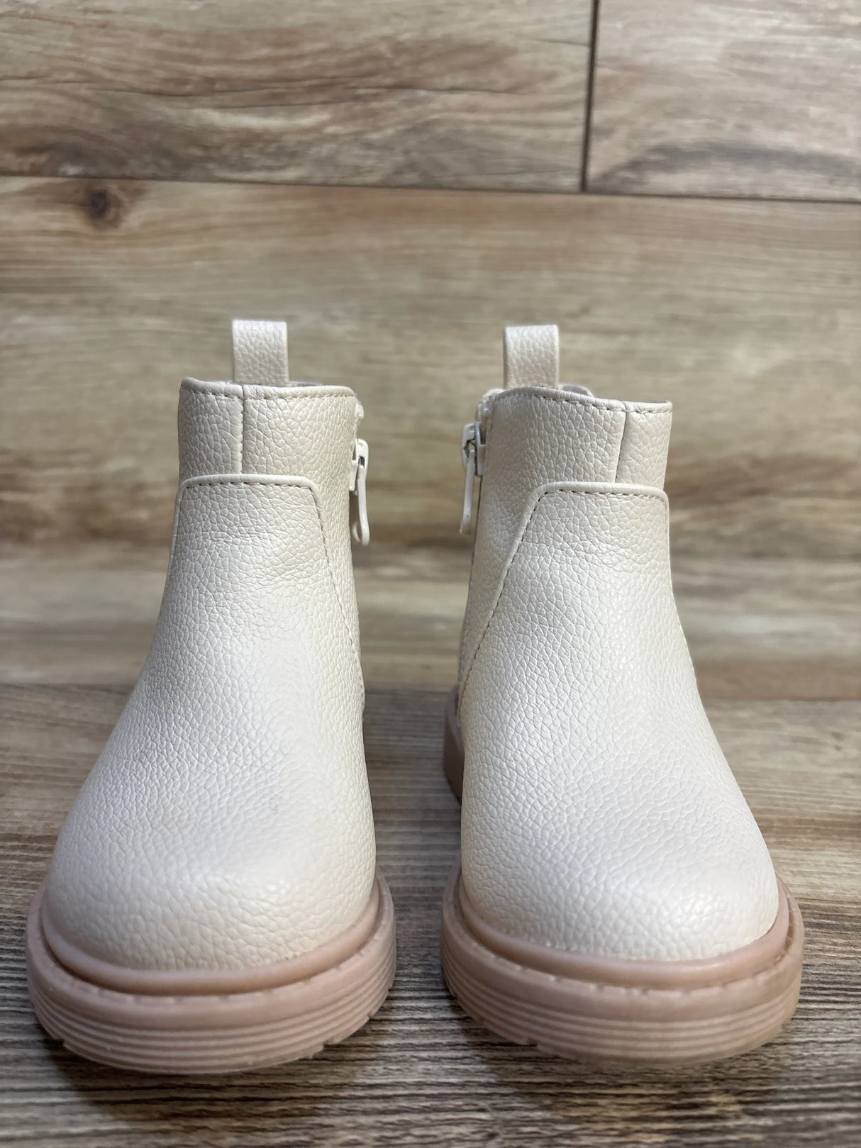 Front view of Cat & Jack Chelsea toddler boots in beige showing side zipper and pink rubber sole on wood floor background