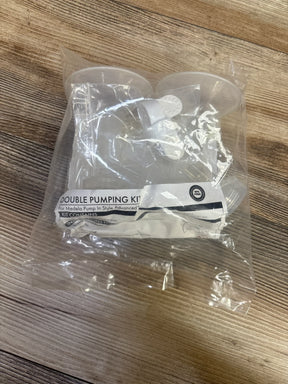 Angled view of Medela double pumping kit showing two clear breast shields and tubing in sealed plastic bag on wood tabletop