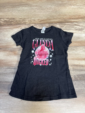 Black kids t-shirt with Glinda Wicked graphic and text, laid flat on wood background