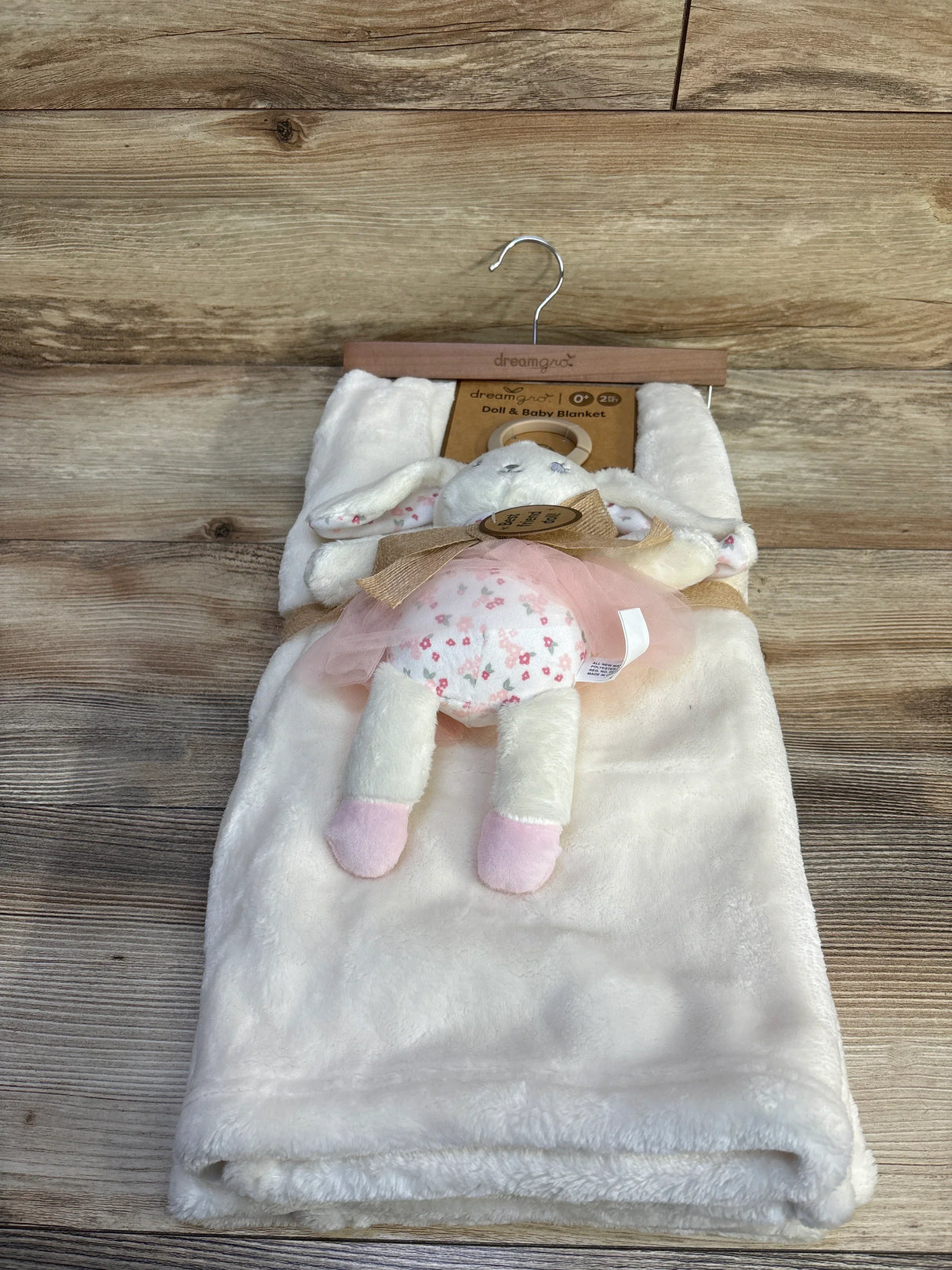 Front view of new DreamGro doll and baby blanket white bunny set showcasing plush bunny doll in floral skirt with hangtag on wood plank floor