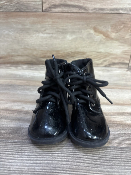 Front view of black patent leather sparkly ankle boots with black laces on a wood floor