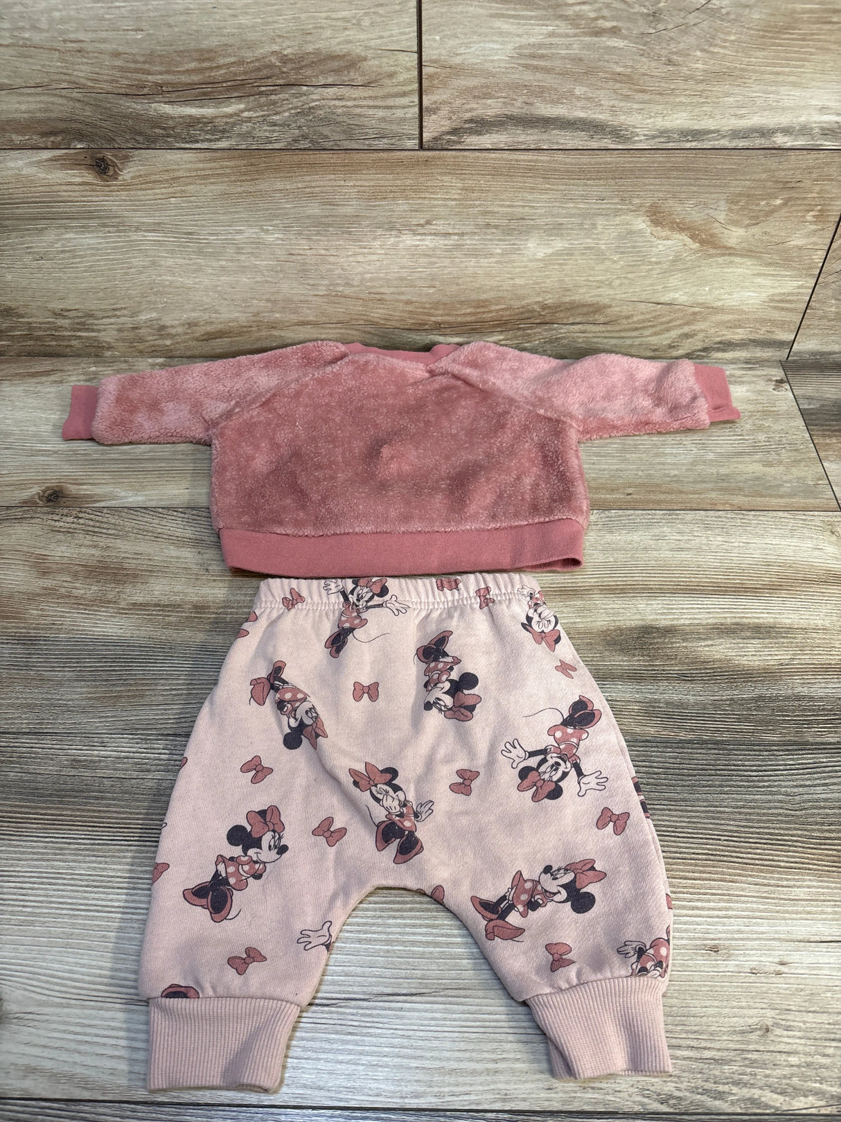Pink toddler outfit with fuzzy sweatshirt and Minnie Mouse patterned pants on wood background
