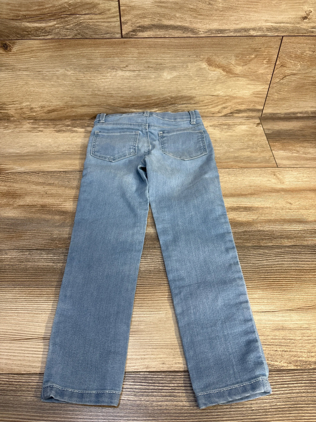Light wash kids jeans with cuffed hems, laid flat on wood floor for resale
