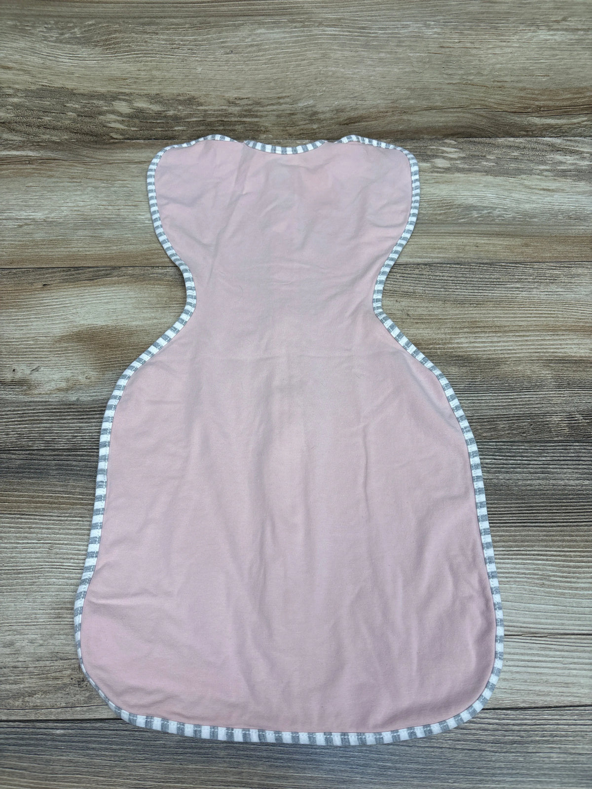 Top view of a pink Love To Dream Swaddle Up Stretch Cotton swaddle sack showcasing striped trim on a wood-grain surface
